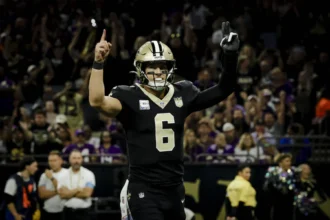 Tyler Shough, Quarterback der New Orleans Saints, steht mit erhobenen Armen neben Tyler Shough auf dem Spielfeld.