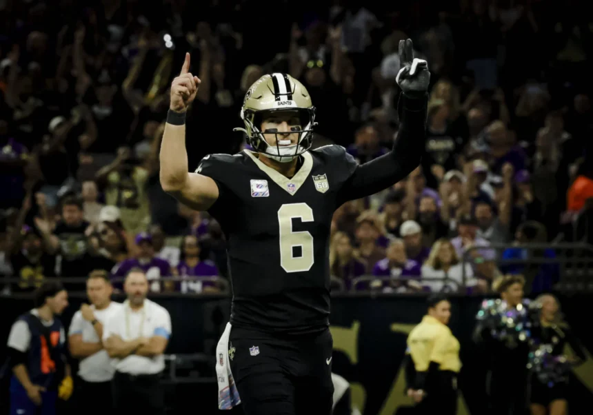 Tyler Shough, Quarterback der New Orleans Saints, steht mit erhobenen Armen neben Tyler Shough auf dem Spielfeld.