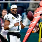 Jalen Hurts steht in seinem Trikot der Philadelphia Eagles mit einem Football an der Seitenlinie.
