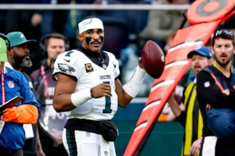 Jalen Hurts steht in seinem Trikot der Philadelphia Eagles mit einem Football an der Seitenlinie.