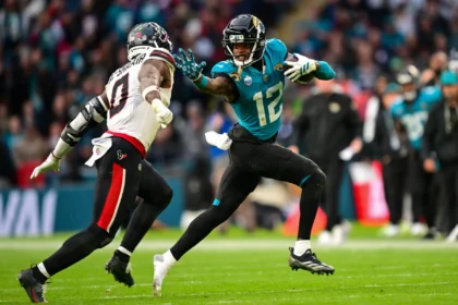Travis Hunter - Ein Spieler der Jacksonville Jaguars in einem türkisfarbenen Trikot läuft mit dem Ball und wird von einem Verteidiger der Houston Texans verfolgt.