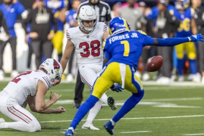 Chad Ryland - Ein Spieler der Arizona Cardinals in weißer Spielkleidung schießt den Ball, während ein Teamkollege kniet und ein Spieler in blau-gelber Spielkleidung versucht, den Schuss zu blocken.