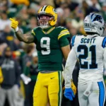 Chrstian Watson - Ein Spieler der Green Bay Packers zeigt neben einem Spieler der Carolina Panthers im weißen Trikot mit dem Namen Scott und der Nummer 21 auf das Spielfeld.