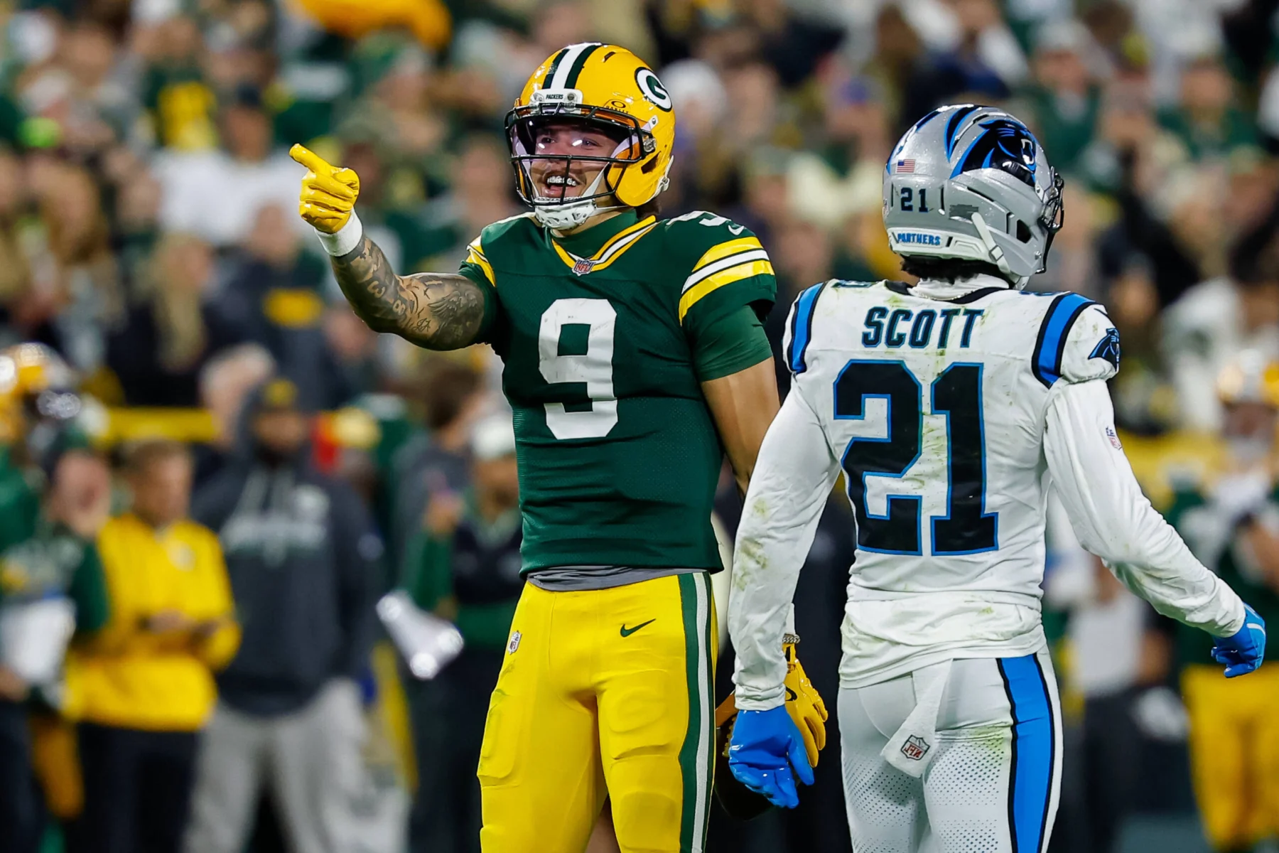 Chrstian Watson - Ein Spieler der Green Bay Packers zeigt neben einem Spieler der Carolina Panthers im weißen Trikot mit dem Namen Scott und der Nummer 21 auf das Spielfeld.