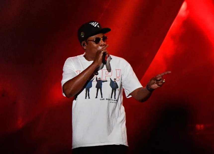 Jay-Z tritt beim Super Bowl LXI auf der Bühne auf und trägt eine Sonnenbrille, eine schwarze Baseballkappe sowie ein weißes T-Shirt mit einem Beatles-Motiv.