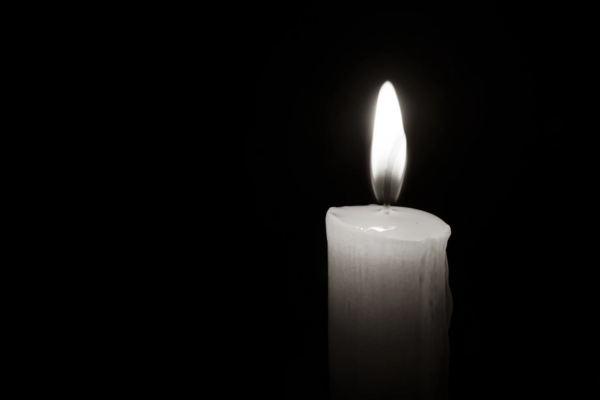 Jeremiah Kelly - NFL - Mason Alexander - Eine einzelne weiße Kerze, an deren Seite geschmolzenes Wachs heruntertropft, brennt hell vor einem pechschwarzen Hintergrund. Die Flamme ist gleichmäßig und leuchtend, wirft einen sanften Schein um die Kerze und beleuchtet ihre wachsartige Oberfläche. Der starke Kontrast, ähnlich wie Jim Ottos Vermächtnis als Mr. Raider, betont das zarte Licht der Kerze. Diese Beschreibung wurde automatisch generiert.