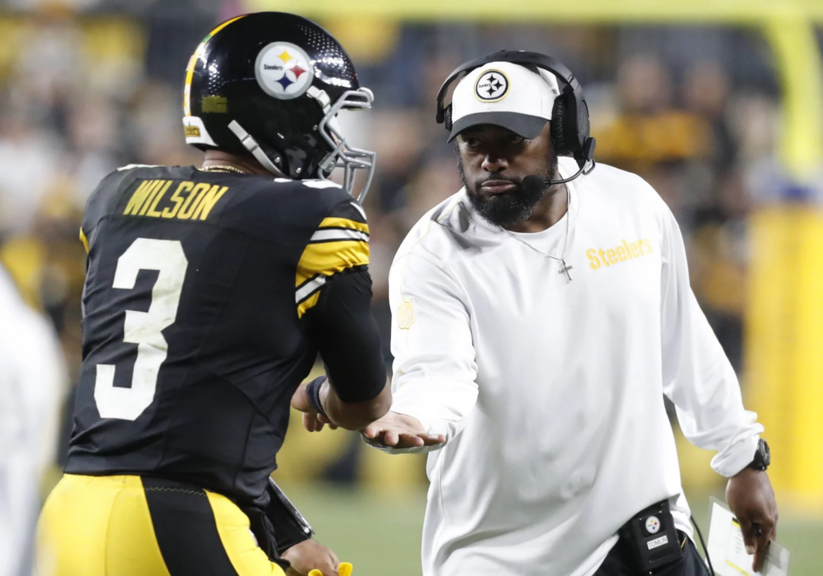 FootballR - NFL - Ein Spieler der Pittsburgh Steelers mit der Trikotnummer 3 namens Russell Wilson erhält während der NFL Woche 7 einHigh Five von Mike Tomlin. Der Trainer, in einem weißen Steelers-Shirt und einer schwarzen Kappe, wirkt konzentriert und hält die Karte mit seiner rechten Hand auf dem Footballfeld, mit verschwommenen Zuschauern im Hintergrund. Diese Beschreibung wurde automatisch generiert.