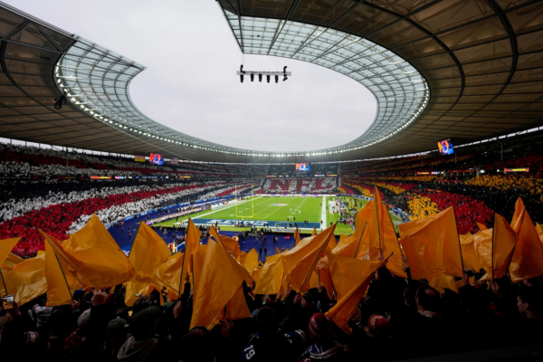 Woche 10 Recap - Ein vollbesetztes Berliner Stadion mit einem geschwungenen Dach und einem Fußballfeld in der Mitte strotzt vor Energie. Die Fans schwenken gelbe Fahnen im Vordergrund, während andere rote, weiße und schwarze Karten in der Hand halten und so ein farbenfrohes Bild unter einem bewölkten Himmel schaffen. Diese Beschreibung wurde mit der FootballR KI automatisch generiert.