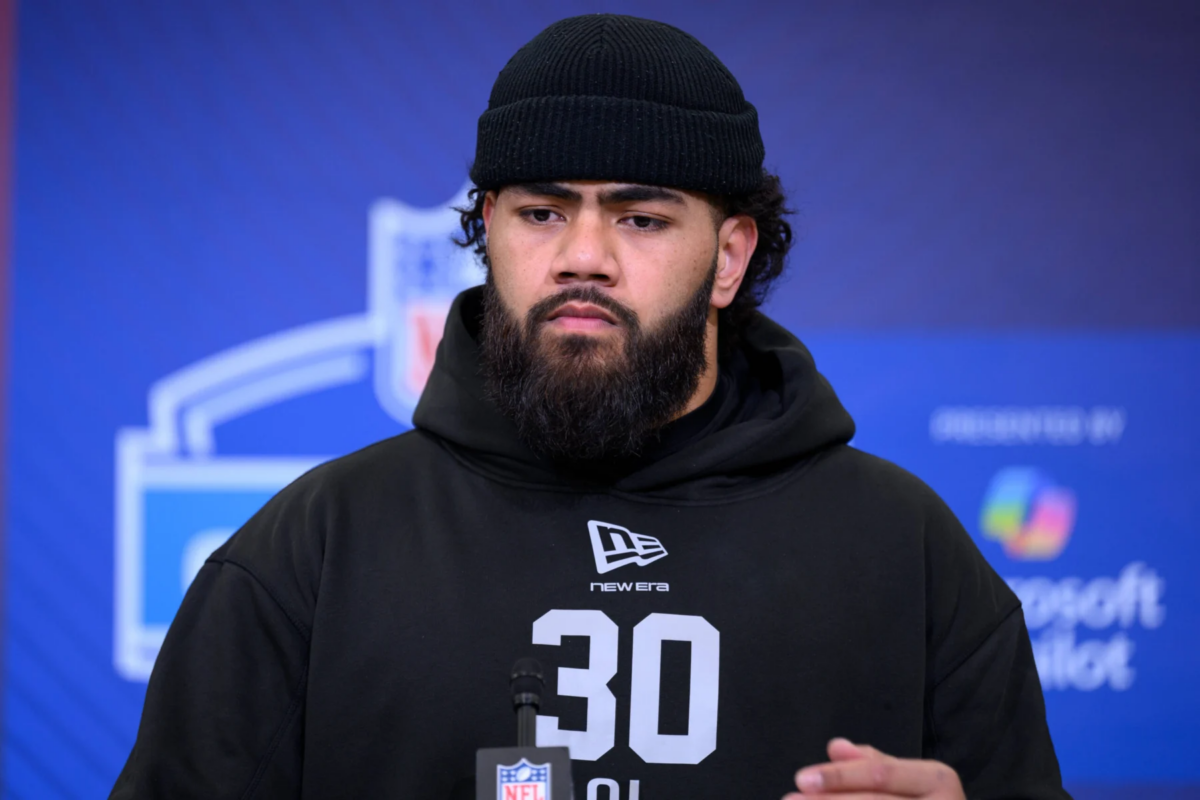 Ein Mann mit Bart und schwarzer Mütze, der einen schwarzen Kapuzenpulli mit der Nummer 30 trägt, steht bei einer Veranstaltung vor einer Kulisse für den NFL Draft 2026. Alt-Text wurde KI-generiert.