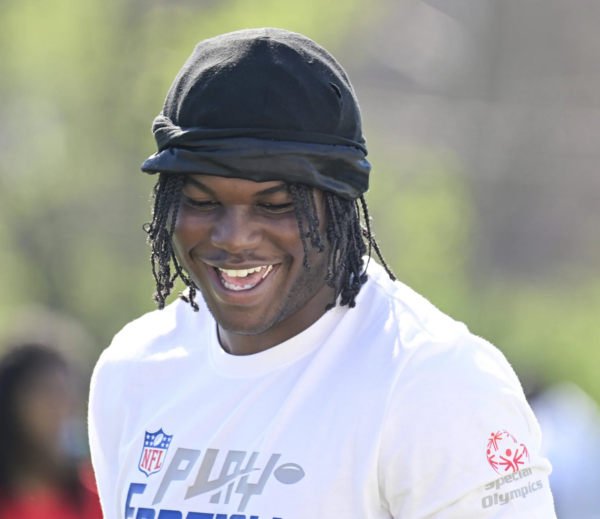 David Bailey - Eine Person, die eine schwarze Kopfbedeckung und ein weißes NFL-Trikot mit einem Special Olympics-Logo trägt, lächelt an einem sonnigen Tag im Freien und inspiriert künftige Edge Rusher im Vorfeld des NFL Draft 2026. Alt-Text wurde KI-generiert.