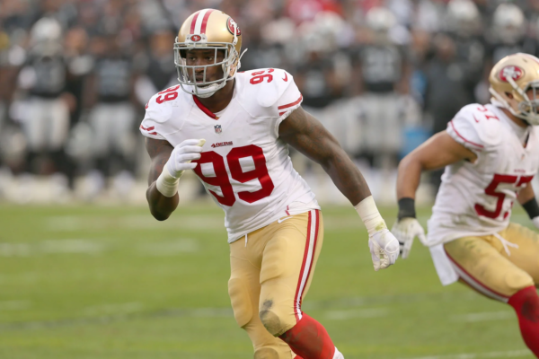 Aldon Smith, der das weiß-rote Trikot der San Francisco 49ers mit der Nummer 99 trägt, rennt während eines Spiels über das Spielfeld. Alt-Text wurde KI-generiert.