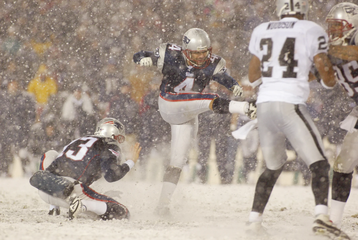 Adam Vinatieri - Ein Footballspieler zeigt die Präzision eines Adam Vinatieri, als er während eines verschneiten Spiels im Schatten der Alpen ein Field Goal schießt, während seine Teamkollegen den Ball halten und die gegnerischen Spieler versuchen, den Schuss zu blocken. Alt-Text wurde KI-generiert.