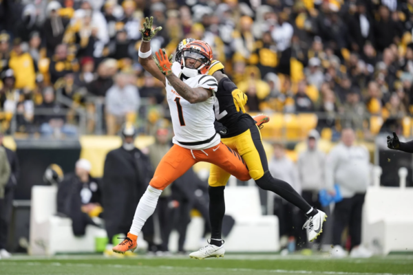 Ein Footballspieler in einem weiß-orangefarbenen Trikot versucht, einen Pass zu fangen, während er auf dem Spielfeld während eines NFL-Spiels von einem Spieler in einem schwarz-gelben Trikot eng gedeckt wird. Dabei können „Jubelstrafen“ – also Strafen für Jubelgesten – dem Geschehen zusätzliche Dramatik verleihen. Alt-Text wurde KI-generiert.