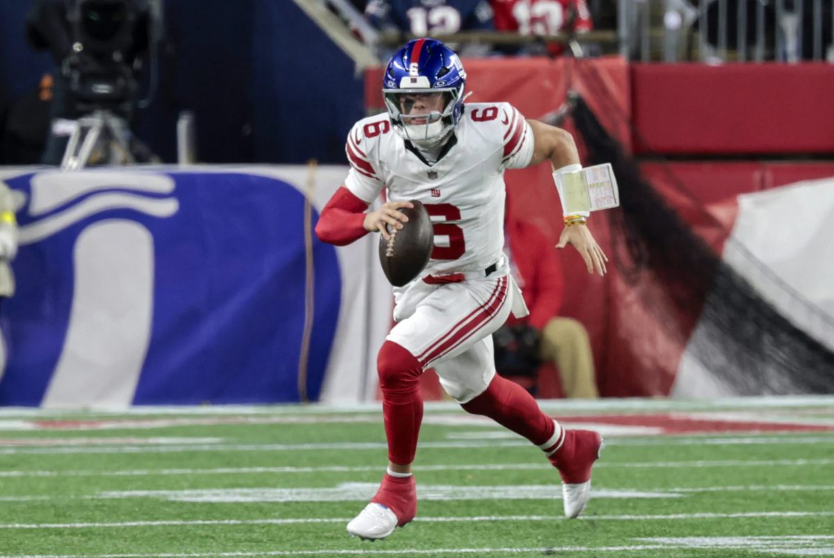 Jaxson Dart - Ein Spieler der Giants in einem weiß-roten Trikot sprintet während eines Spiels auf einem grünen Rasen mit dem Ball los. Alt-Text wurde KI-generiert.