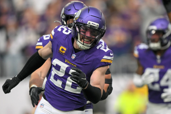 Ein Footballspieler in einem violetten Trikot und Helm der Minnesota Vikings läuft während eines Spiels über das Spielfeld, im Hintergrund sind seine Teamkollegen zu sehen, während der Bericht „Vikings holen Harrison Smith“ die starke Defensivaufstellung des Teams unterstreicht. Alt-Text wurde KI-generiert.