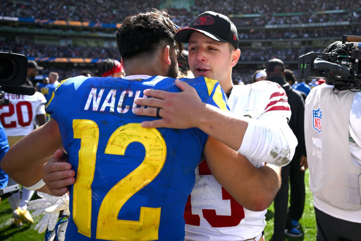 Brock Purdy - Puka Nacua - Zwei American-Football-Spieler gegnerischer Mannschaften umarmen sich nach einem Spiel auf dem Spielfeld, umringt von anderen Spielern und einem Kameramann, während die 49ers den trägen Rams einen bitteren Abend bescheren. Alt-Text wurde KI-generiert.