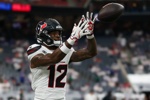 Nico Collins - Ein Footballspieler in einem weißen Trikot der Houston Texans mit der Nummer 12 fängt während eines Spiels einen Football, im Hintergrund sind verschwommene Stadionplätze zu sehen – dies unterstreicht den Moment, in dem Collins von den Texans gegen die Bengals ausfällt. Alt-Text wurde KI-generiert.