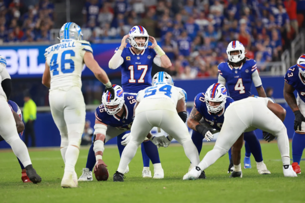 Josh Allen, der Quarterback der Buffalo Bills, erzielt 5 Touchdowns, während er sich darauf vorbereitet, den Snap zu empfangen, und dabei den Verteidigern der Carolina Panthers gegenübersteht. Alt-Text wurde KI-generiert.
